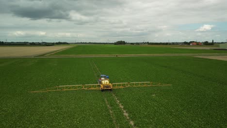 Fliegen-Einer-Drohne-Hinter-Einem-Traktor-Mit-Gezogener-Feldspritze,-Der-Auf-Einem-Bebauten-Feld-Fährt