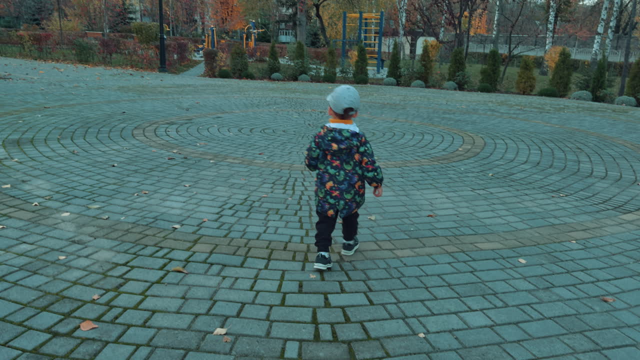 Cute little kid wearing cap, jacket and pants walks outdoors. Baby boy spending time in autumn park.