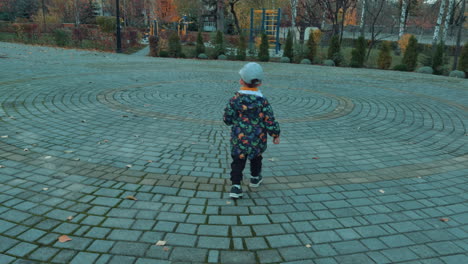 cute little kid wearing cap, jacket and pants walks outdoors. baby boy spending time in autumn park.