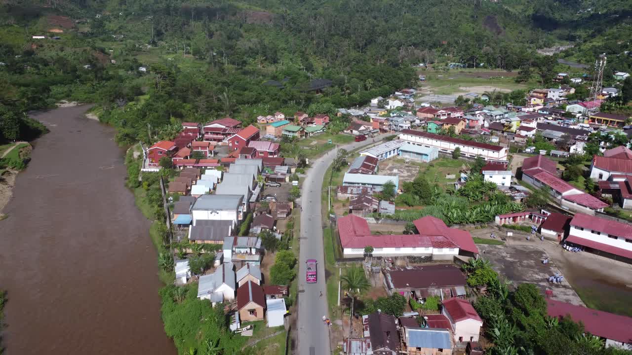 Bus merah muda melaju melintasi desa, kota kecil, dan kota di hutan Madagaskar.