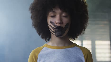 retrato de una mujer afroamericana con una marca de mano en la boca de pie en un garaje vacío