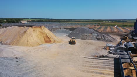 excavator on the quarry. big territory of asphalt factory. piles with sand and rubbles outdoors. aerial view. camera motion up.