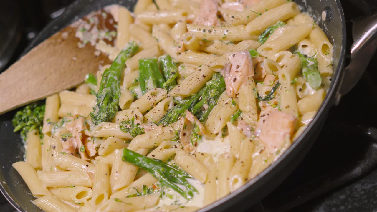 Pushing Shot Towards Creamy Delicious Salmon and Vegetable Broccoli Penne Italian Pasta on Stove with Cracked Black Pepper. Cooking Kitchen Seafood Healthy Eating Footage 4K.