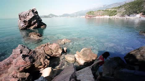 Dama-Caminando-Sobre-La-Costa-Rocosa-Con-Aguas-Realmente-Tranquilas-En-La-Costa-Adriática-En-Montenegro