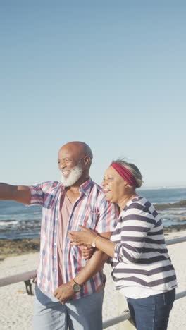 vertical video of senior biracial couple embracing on promenade by the sea, slow motion