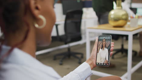 mujer de negocios afroamericana que usa un teléfono inteligente para una videollamada con un colega de negocios biracial
