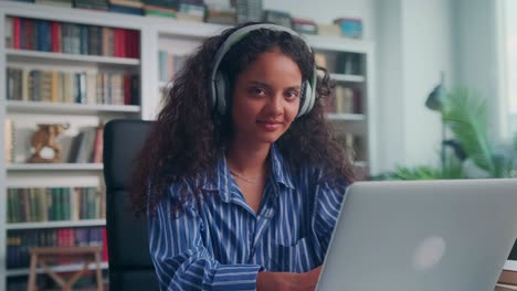 young indian woman works with laptop listening to music in wireless headphones