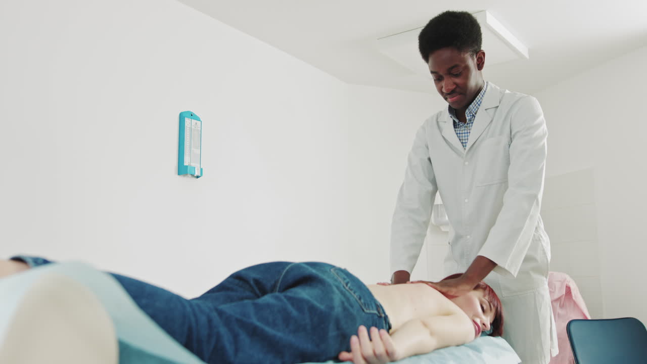 African physiotherapist conducts massage therapy to young female to restore muscle strength at the