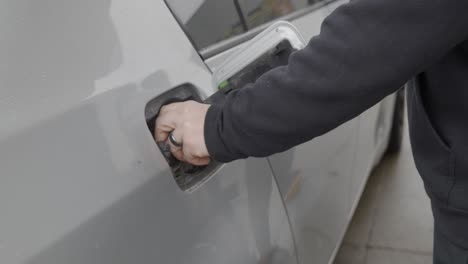 Gas-station-white-caucasian-man-with-wedding-ring-filling-up-silver-car-replacing-gas-cap-and-closing-fuel-tank-cover-and-walking-to-front-of-car