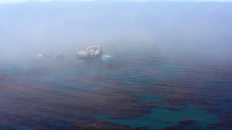 huge rock formations out at sea covered in morning fog