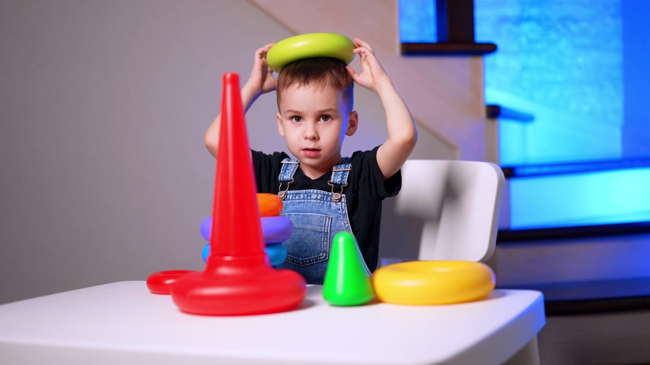 Boy balancing green ring on his head. Blue accent lighting fills the background behind colorful rings and cones.