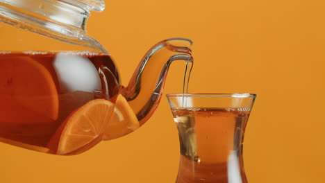 close-up of tea with orange slices being poured from a pitcher into a glass