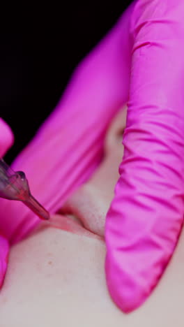 microblading procedure. applying permanent make up tattoo on young girl lips. hands in protective gloves of a cosmetologist doing lips tattoo. close-up. vertical video