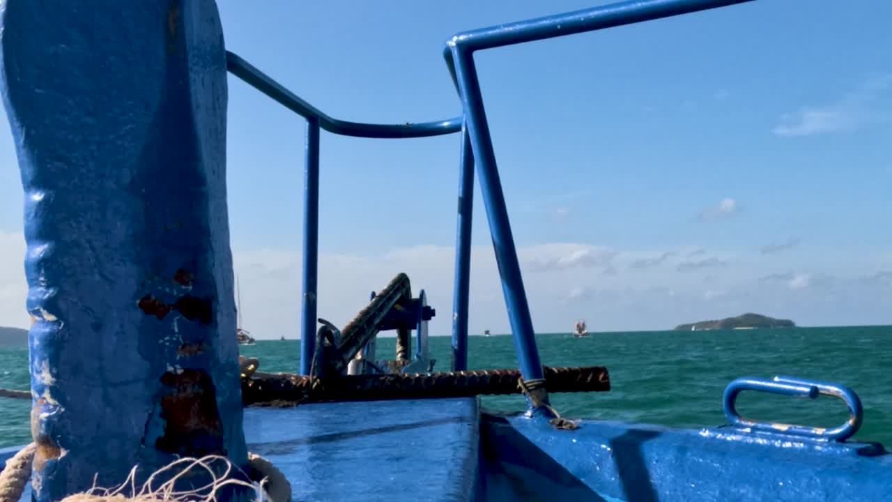 Una perspectiva en primera persona desde la cubierta de un barco azul navegando por tranquilas aguas turquesas bajo un cielo despejado