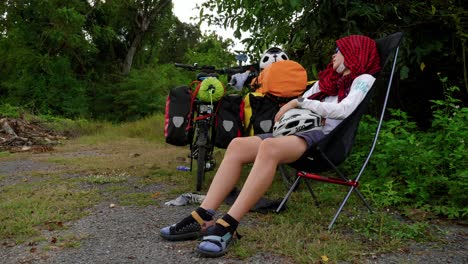 female cyclist resting in chair holding helmet after day of bike riding, thailand