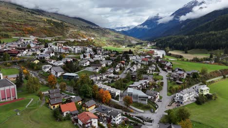 aerial flyover scoul town in switzerland with houses and apartment blocks. swiss community between mountains and cloudscape. sunny fall season day in switzerland. wide shot.