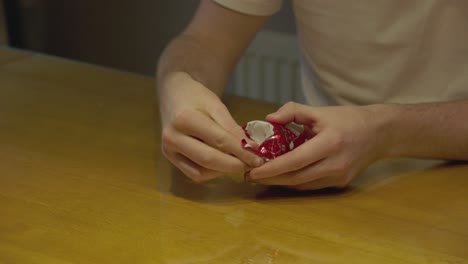 close-up shot of a man wrapping up a small christmas gift at a table