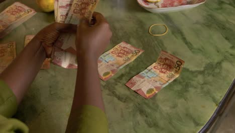 female black woman hands counting ghanaian cedi currency of ghana organising paper bills on table house