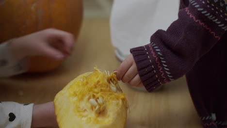 dos niños pequeños quitando las semillas de una calabaza para halloween