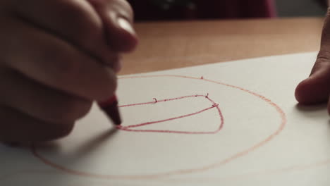 a child drawing a house with a red crayon as the camera tracks left