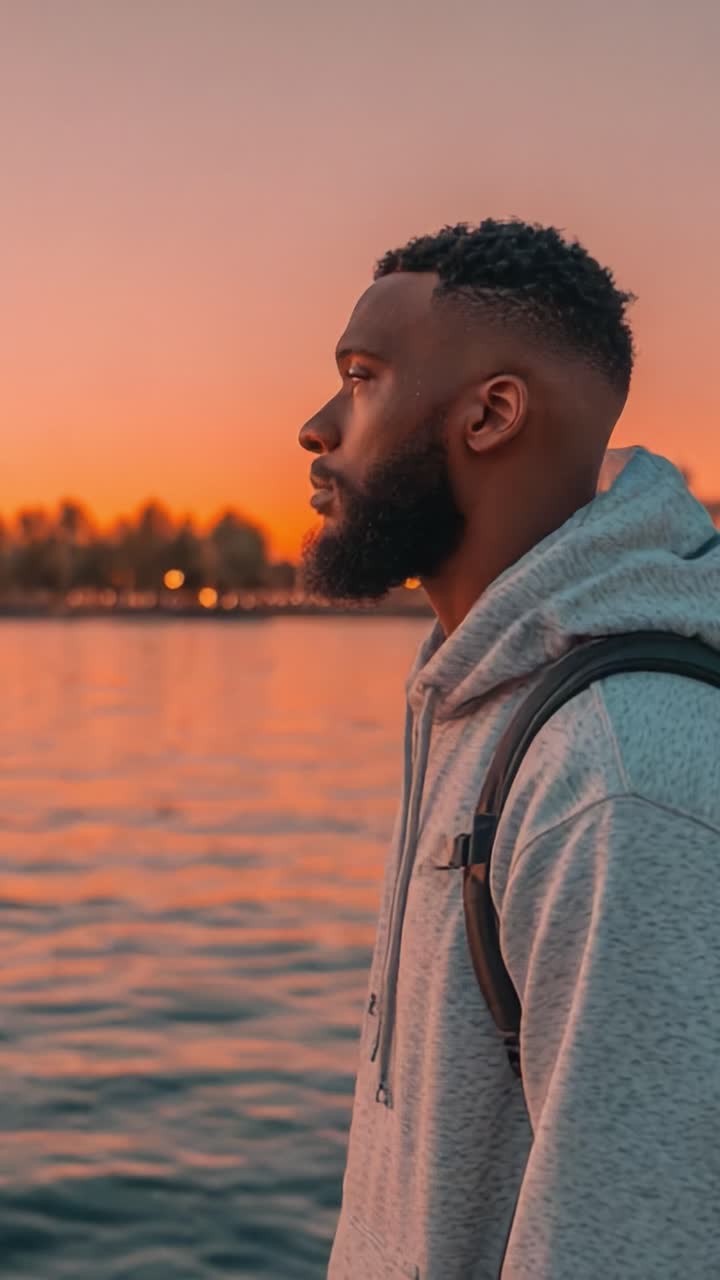 A Reflective Moment at Sunset: A Young Man Contemplates Life by the Water's Edge, Bathed in Warm Orange and Pink Hues of Dusk, Symbolizing Hope and Possibilities