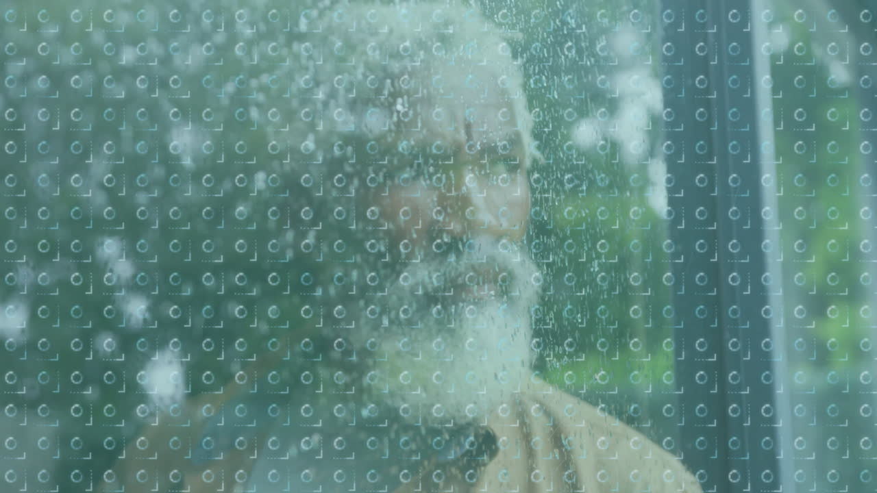 Through rain-covered glass, elderly man with beard looking outside quietly