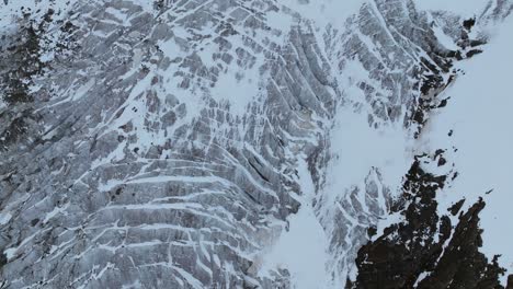 Una-Impresionante-Vista-Desde-Arriba-Captura-Los-Intrincados-Patrones-De-Un-Glaciar-Yuxtapuestos-Contra-Un-Terreno-Montañoso-Accidentado.