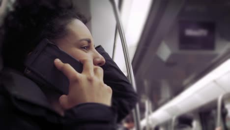 hispanic young woman talking and using mobile phone while traveling in the train or subway