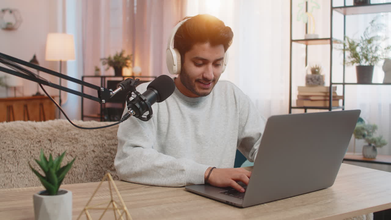 Hindu-Mann benutzt Laptop, um Vlogs aufzunehmen und Online-Streams zu führen, während er zu Hause am Tisch sitzt