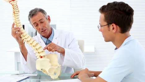 médico maduro hablando con su paciente sobre el modelo de columna vertebral