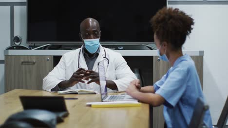 diverse female and male doctors wearing face masks discussing in office