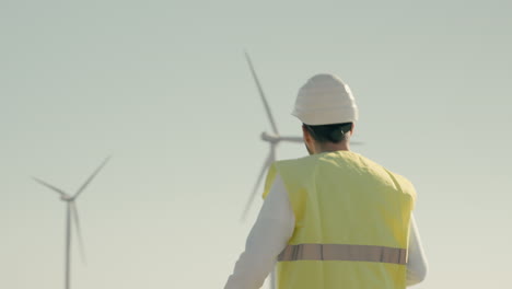 walking through a field of wind turbines, a skilled engineer in a white helmet and reflective vest ensures a sustainable future