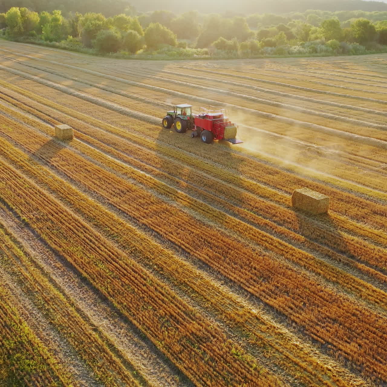 Aerial view of a tractor baling hay in a field during sunset.