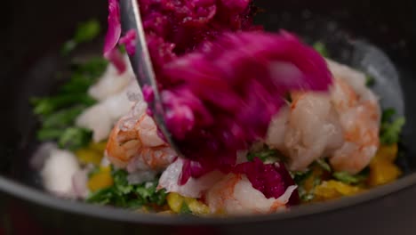 chef prepares cebiche by placing red onion and prawns in a bowl with coriander and yellow pepper