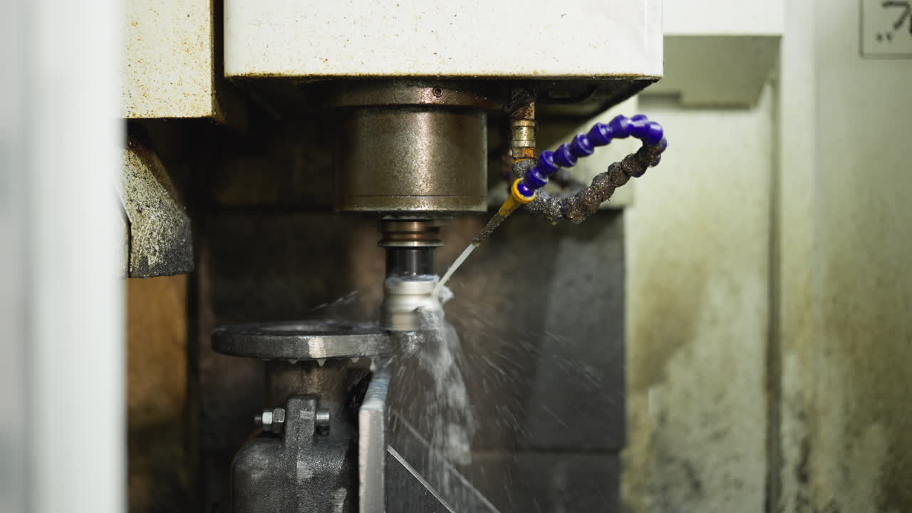 Primo piano di una macchina CNC in funzione con spruzzo di refrigerante su un pezzo di metallo rotante.