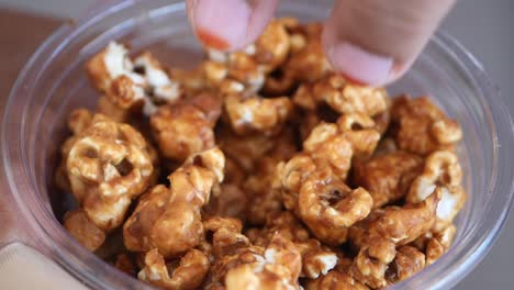 hand picking caramel popcorn from a container