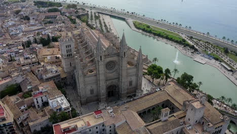 AERIAL:-Palma-Cathedral-Close-Up-shot-in-Daylight,-Blue-Sky-with-Traffic-and-Tourists-on-Tropical-Island-Mallorca,-Spain-on-Sunny-Day-Vacation,-Travel,-Sunny