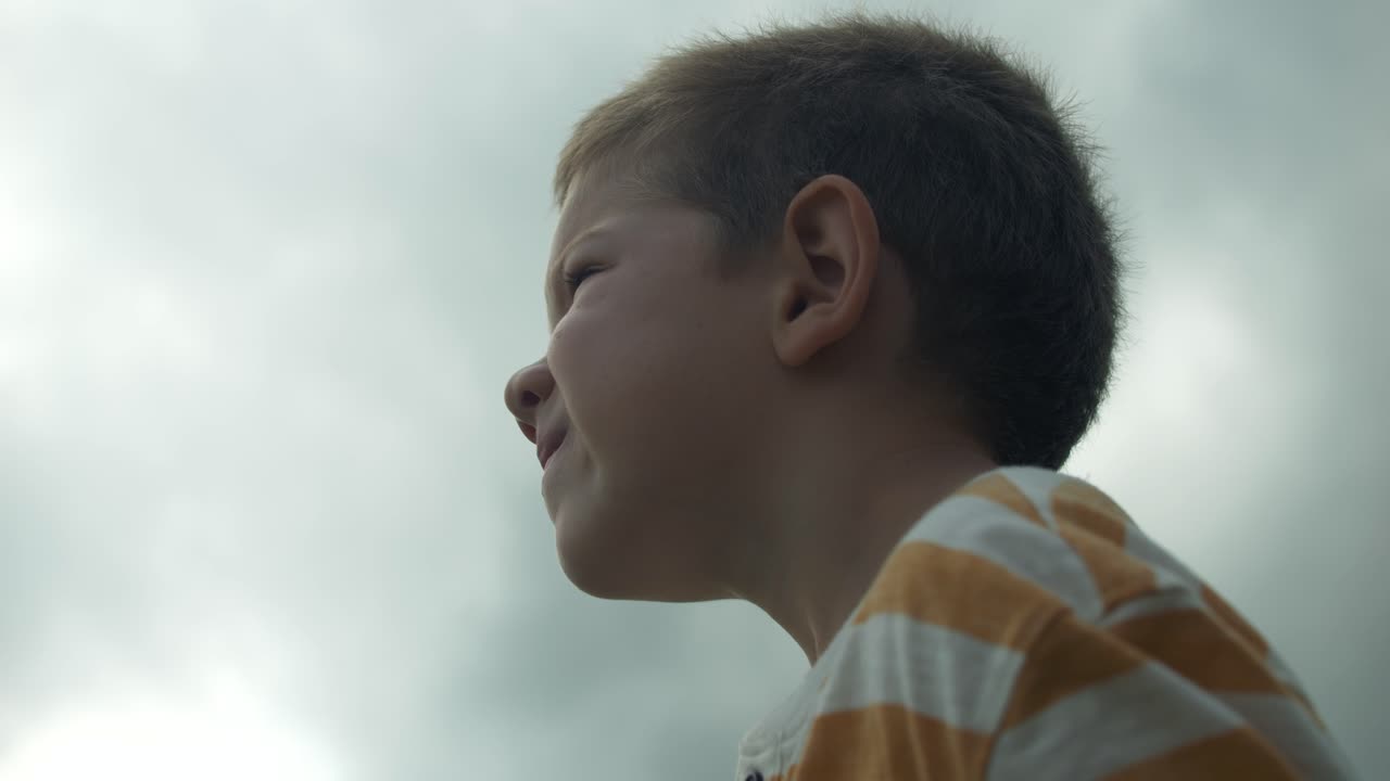 A young boy gazes up at the sky in slow motion, his eyes full of wonder and curiosity. This cinematic footage captures the innocence and imagination of childhood.