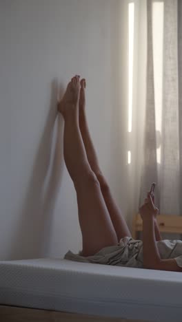 Woman relaxing in bed with legs up the wall