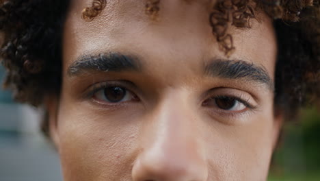 brown eyes man looking camera outdoors extreme closeup. curly teen staring lens