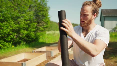 hombre caucásico con un rollo de estera de prevención de malezas para la cama elevada del jardín