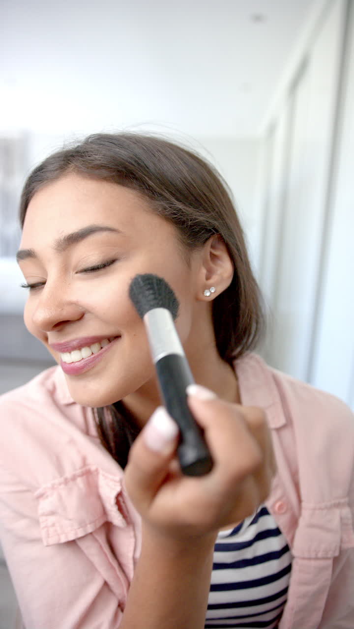 Vertical video: Applying makeup with brush, woman smiling and looking at camera at home