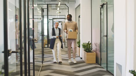 muslim businesswoman accompanies a young man with a box along the corridor to his office