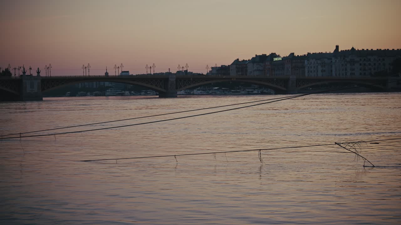serene view of a bridge reflecting in floodwaters, debris scattered along the surface