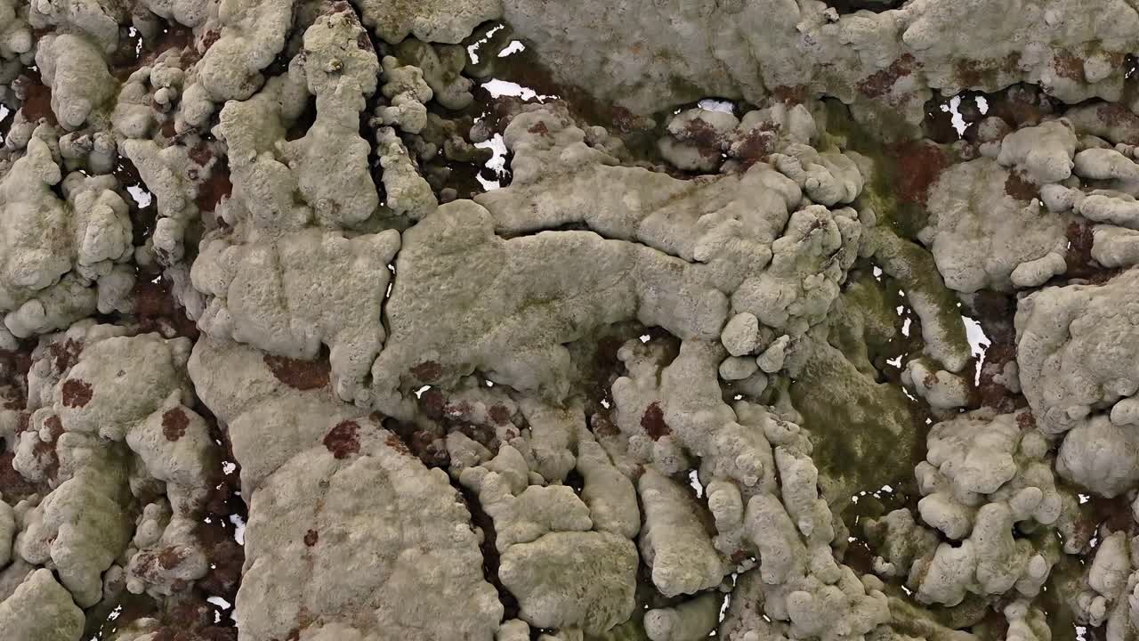 Detailed top-down aerial view of the textured ground within Fjaðrárgljúfur Canyon, Iceland. Patterns of rock, moss, and small pools.