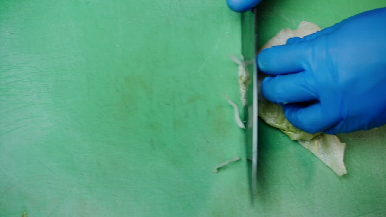 Chef with gloves cutting cabbage on the table, overhead view