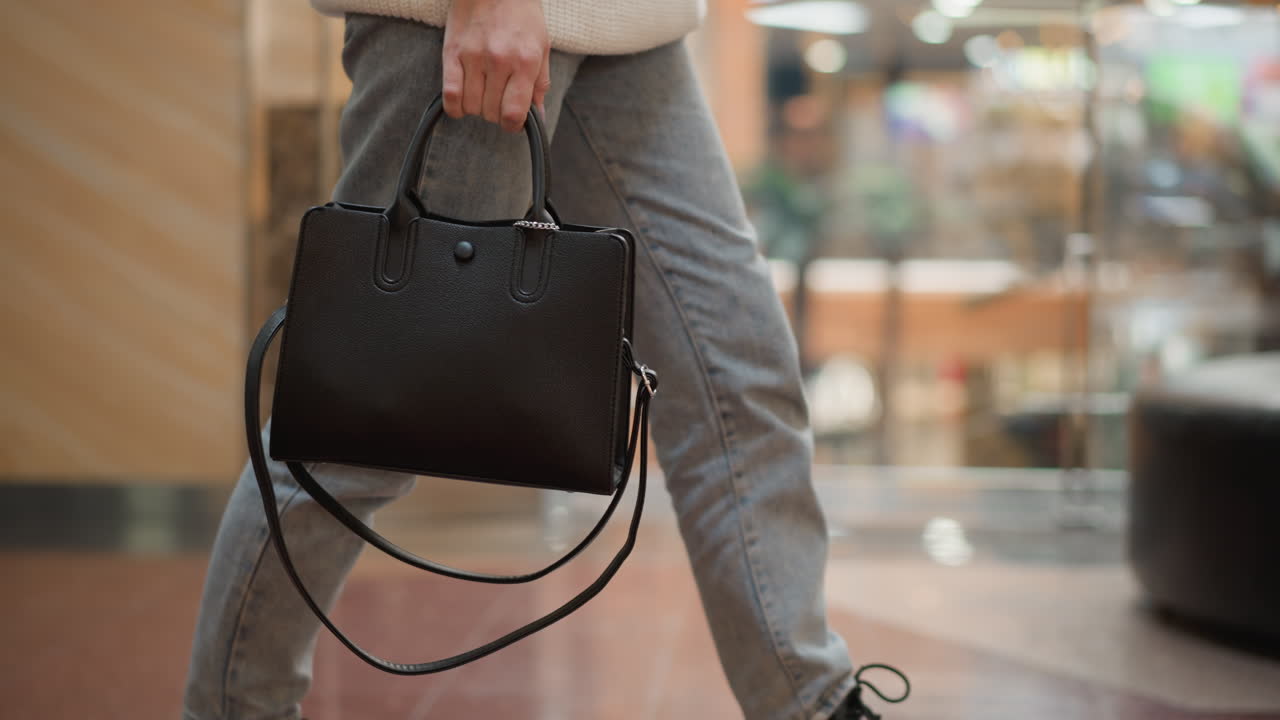 low angle close up of woman wearing denim jeans and chunky black boots carrying bag walking on polished tiled mall floor under bright overhead lights capturing motion and style