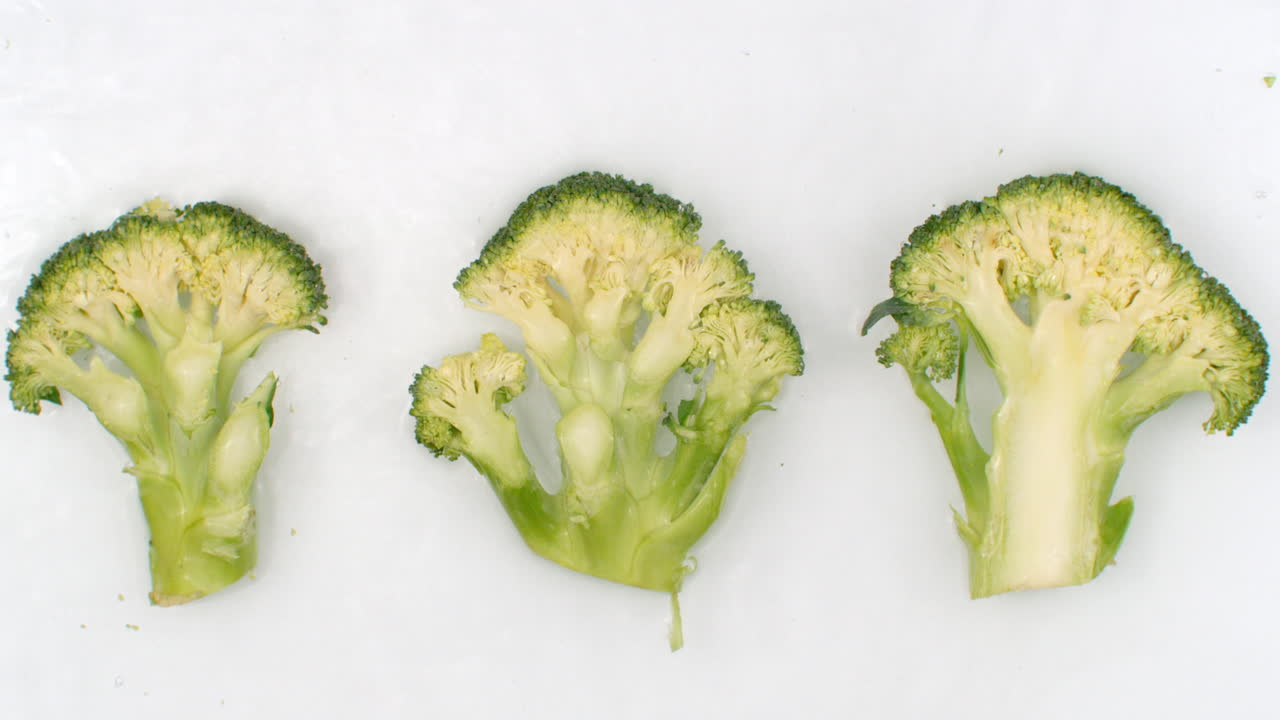 Slow motion water splash on three slices of green broccoli lying on a white background in the water