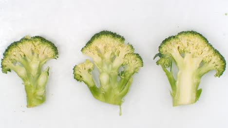 slow motion water splash on three slices of green broccoli lying on a white background in the water