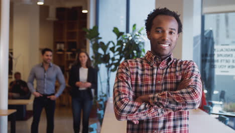 portrait of businessman standing in busy modern open plan office  with colleagues in background